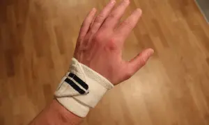 En hand med handledsskydd, kanske för att stödja en svag handled. Skyddet är vitt med mörkblå ränder.