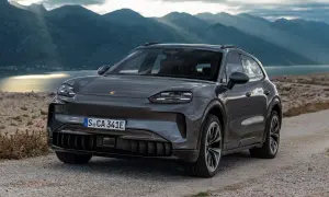 Szary Porsche Cayenne 2025 na kamienistej drodze z widokiem na góry i jezioro.