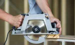Mains d'un bricoleur utilisant une scie pour parquet stratifié, coupant une planche de bois.