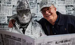 Tomasz Tomaszewski w kapeluszu i płaszczu z gazet. Obok uśmiechnięty mężczyzna w okularach.