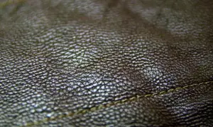 Zbliżenie na fakturę ciemnobrązowej skóry. Real leather to naturalny, trwały materiał, który pięknie się starzeje. Widoczny delikatny szew.