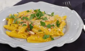 En krämig pasta milanese med mandelspån och färska örter, serverad i en ljusblå skål.