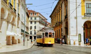 Gul lissabon spårvagn på kullerstensgata, omgiven av gul och vit arkitektur.