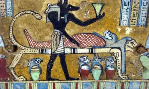 Anubis, bóg z głową szakala, stoi przy katafalku z mumią. W ręku trzyma naczynie, a obok stoją urny z głowami zwierząt.