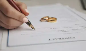 Dłoń z piórem podpisuje dokument, obok leżą obrączki. Rozdzielność majątkowa koszt to ważna decyzja.