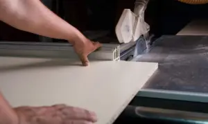 Precyzyjne cięcie płyty MDF na pile stołowej. Ręce stolarza prowadzą materiał do obracającego się ostrza.