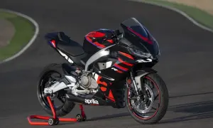 Czarny motocykl sportowy Aprilia na czerwonym stojaku na torze wyścigowym.