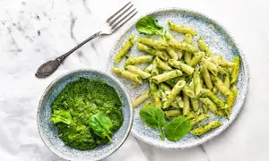 Penne z domowym pesto ze szpinaku, podane w miseczce i na talerzu, z widelcem obok.
