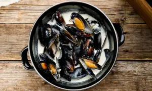 Un plat de moules à la crème, prêtes à être dégustées sur une table en bois rustique.