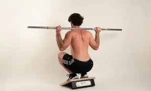 Mann mit lockigem Haar macht eine Kniebeuge mit Langhantel auf einem Trainingsgerät.