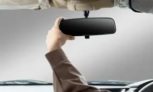 Main d'un conducteur ajustant le rétroviseur intérieur de sa voiture. Apprenez comment emboîter un rétroviseur intérieur pour une meilleure visibilité.
