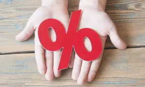 Dłonie trzymające duży czerwony znak procentu, symbolizujący odsetki od niezapłaconej faktury.