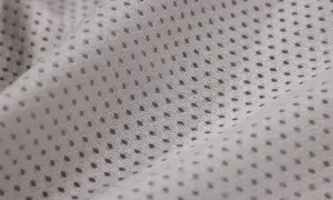 Jasnoszara tkanina siateczka z drobnymi, regularnymi otworami. Materiał jest pofałdowany, tworząc miękkie linie.