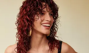 Donna sorridente con splendidi capelli mogano ricci e bagnati, che le incorniciano il viso.