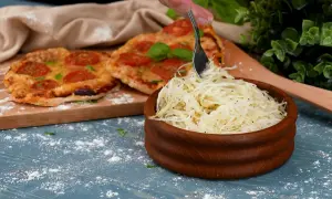 En skål med krispig pizzasallad bredvid en pizza med tomater. Perfekt för ditt pizzasallad recept!