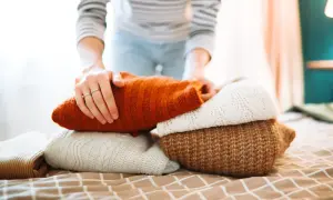 Hände falten warme Pullover. Der Wollprogramm-Waschgang ist abgeschlossen, die Kleidung ist bereit für den Schrank.
