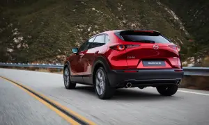 Röd Mazda CX-30 hybrid på en slingrig väg i bergen. Testkörning av den nya modellen.