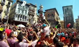 Multitud celebra cuando son vaquillas en Teruel. Gente en una plaza con edificios históricos, algunos subidos a un monumento.