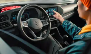 Interni moderni del Volkswagen Caddy: un utente interagisce con il touchscreen centrale, mentre il volante e il cruscotto digitale sono ben visibili.