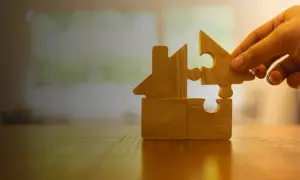 Mano aggiunge un pezzo a un puzzle a forma di casa, simboleggiando una casa in comproprietà tra fratelli e madre.