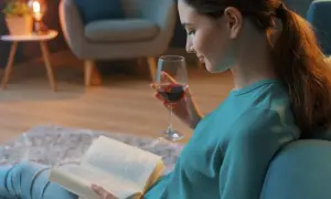 Kobieta z kieliszkiem wina czyta książki. Może to być jedna z fascynujących powieści Joanny Jax, która wciąga w swój świat.