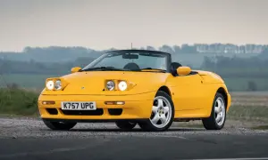 Gul Lotus Elan M100 cabriolet parkerad på grusväg med dimmig bakgrund.