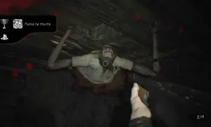Zdobądź osiągnięcie "Packa na muchy" w Resident Evil 7. Potwór wisi na suficie, a gracz celuje bronią.