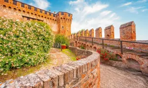 Un sentiero in mattoni conduce al **belvedere ostrense**, con un muro di rose bianche e la rocca medievale sullo sfondo.