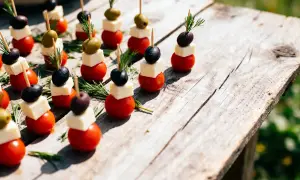 Des mini brochettes apéritives sans cuisson : tomates cerises, dés de fromage, olives noires et vertes, garnies de romarin frais sur une table en bois.