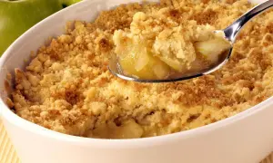Un délicieux crumble aux pommes, parfait pour suivre la recette de Cyril Lignac. La cuillère en argent révèle des morceaux de pommes fondantes sous une pâte croustillante.
