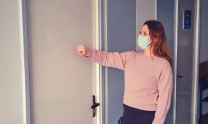 Kobieta w maseczce puka do drzwi gabinetu. Zastanawia się, czy do ginekologa potrzeba skierowania.