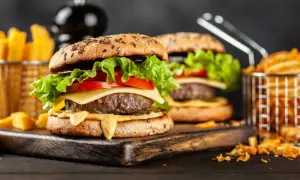 Dwa soczyste burgery z serem, sałatą i pomidorem, podane z frytkami w koszyczkach.
