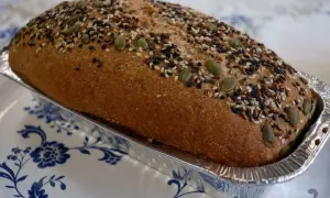 Chleb Ezechiela w formie bochenka, posypany pestkami dyni, sezamem i siemieniem lnianym, w aluminiowej foremce.