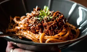 Ein Teller Spaghetti Ragu, garniert mit Parmesan und frischen Kräutern, wartet darauf, genossen zu werden.
