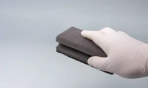Ręka w białej rękawiczce trzyma magiczne gąbki, czyszcząc błyszczącą powierzchnię.