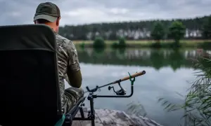 Wędkarz siedzi na krześle nad jeziorem, gotowy do dalekich rzutów z użyciem feeder do dalekich rzutów.