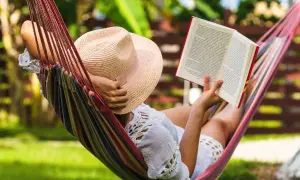 Une personne lit un livre dans un hamac coloré, profitant d'un des 7 types de repos sous un chapeau de paille.