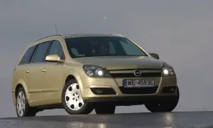 Złoty Opel Astra H kombi z włączonymi światłami. Przód samochodu z wyraźnie widocznymi żarówkami.