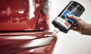 Hand drückt 3M-Paste auf zerkratzten roten Autolack. So lassen sich auto kratzer entfernen und der Glanz wiederherstellen.
