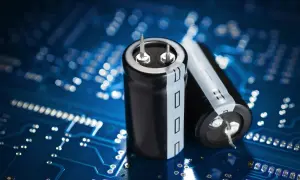 Dwa kondensatory elektrolityczne na tle niebieskiej płytki drukowanej. Różne rodzaje kondensatorów są kluczowe w elektronice.