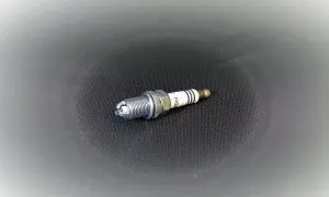 Una bujía lista para el cambio. Su diseño metálico y cerámico blanco con franjas negras indica su función en el motor.
