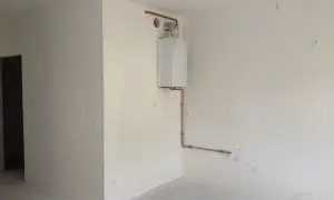 Widok na pomieszczenie, gdzie widać jak zabudować piec gazowy. Biały piec wiszący na ścianie, połączony miedzianymi rurkami z instalacją.