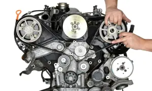 Mechanik demonstruje wymianę rozrządu w silniku samochodowym, wskazując na pasek i koła zębate.