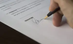 Dłoń podpisuje dokument, co może oznaczać zawarcie lub odstąpienie od umowy.
