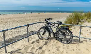 Dwa rowery stojące na piaszczystej plaży, z widokiem na morze i błękitne niebo.