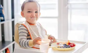 Kleiner Junge mit Heidelbeeren und Joghurt im Gesicht, der an seinem Becher nippt.