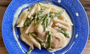 Penne z piersią kurczaka i szparagami w kremowym sosie, podane na niebieskim talerzu.