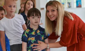 Eine Frau in Rot lächelt und legt ihre Hand auf die Schulter eines Jungen mit Down-Syndrom. Man darf behindert sagen, wenn man über Inklusion spricht.