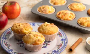 Saftige apfelmuffins ohne zucker, frisch gebacken und auf einem Teller mit Blumenmuster arrangiert. Daneben liegen Äpfel und Zimt.