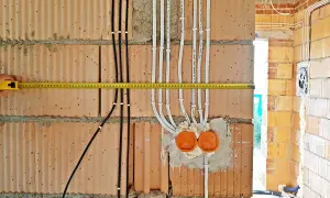 Instalacja elektryczna w domu w trakcie budowy. Widoczne przewody, puszki i miarka.